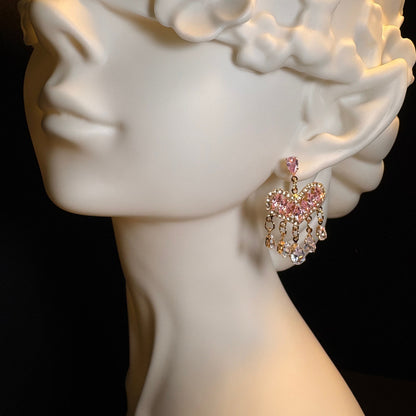 Close-up of pink zircon heart dangle earrings with gold-tone details