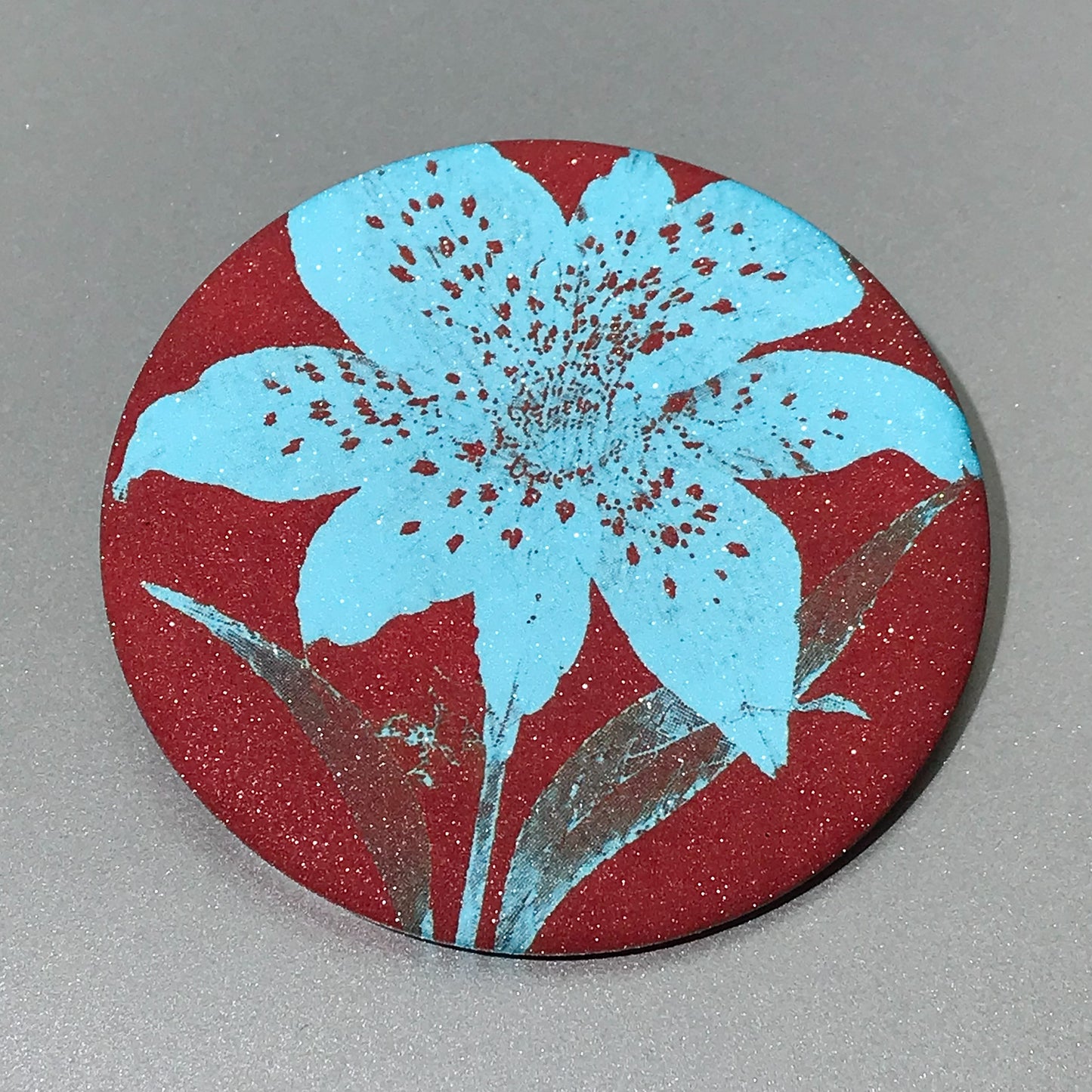 Round pocket mirror with bright aqua lily-style flower and matte-touch back