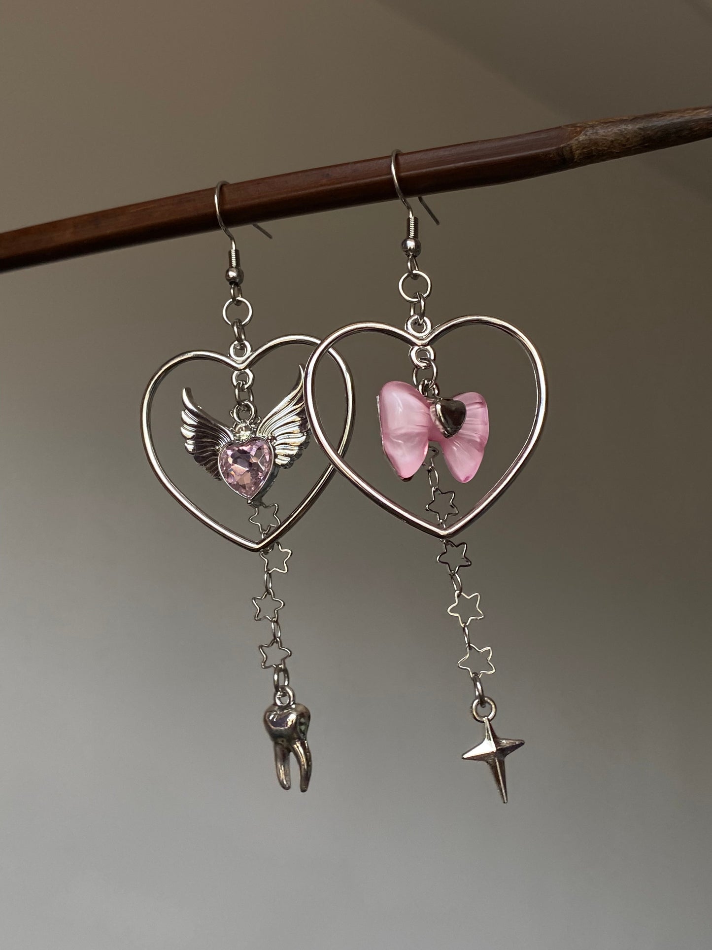 Close-up of asymmetrical heart charm earrings with pink bow and small tooth charm